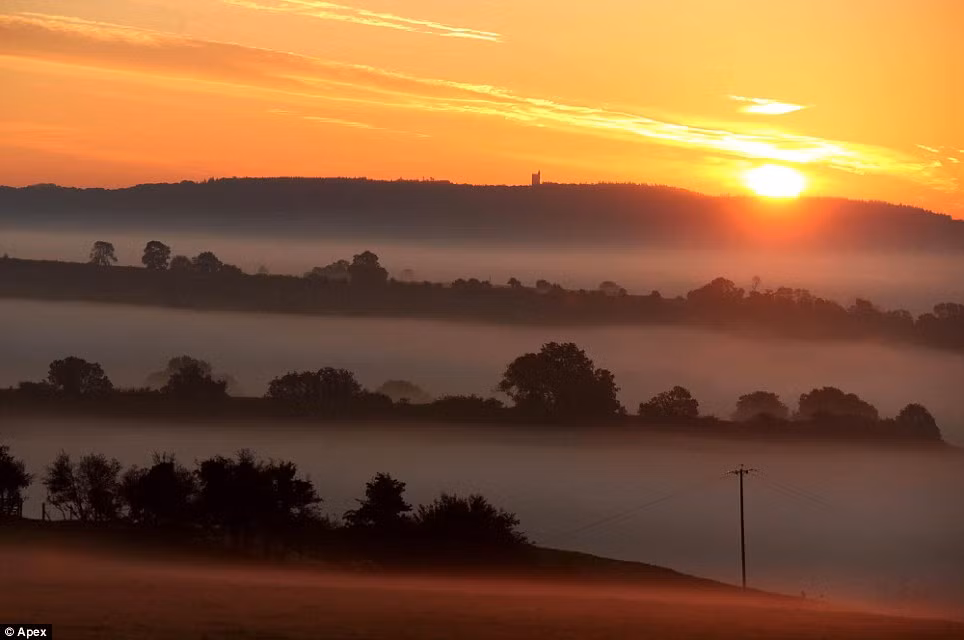 Bầu trời trên cánh đồng gần Bruton, Somerset được nhuộm màu vàng cam rực rỡ trong buổi bình minh.