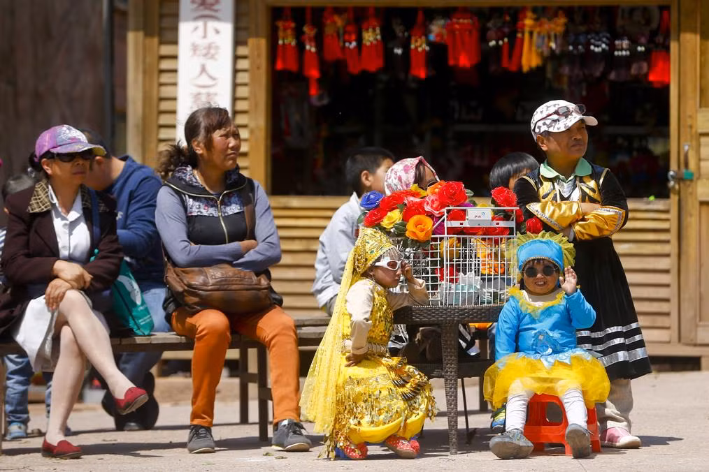 Khách du lich (trái) chăm chú ngồi xem một chương trình tạp kỹ tại công viên theo chủ đề vương quốc người lùn bên cạnh các cư dân ở đây.