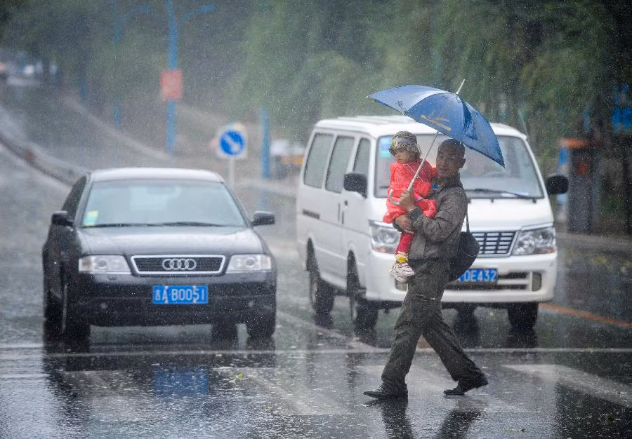 Một người đàn ông bế con với trang phục mùa đông đi dưới trời mưa ở thành phố Trường Xuân.