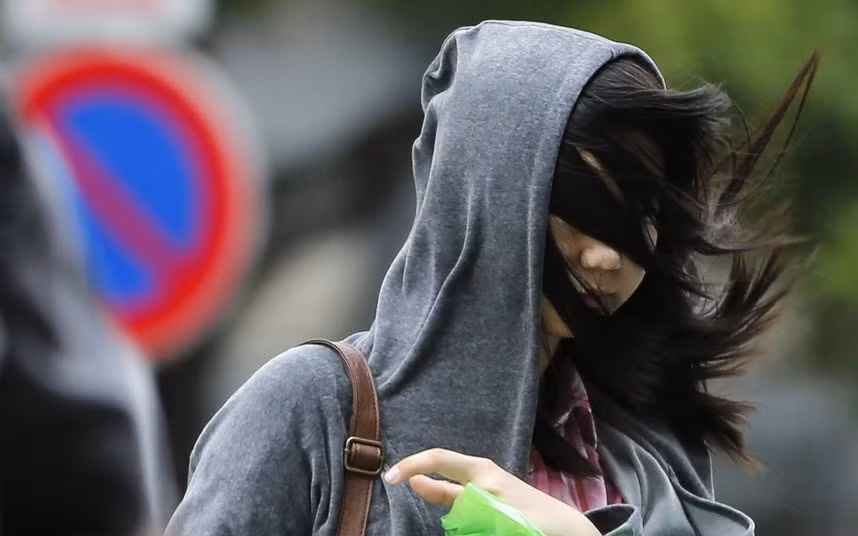 Tóc của một phụ nữ bị gió thổi bay che kín mặt khi đi trên đường phố ở Tokyo.