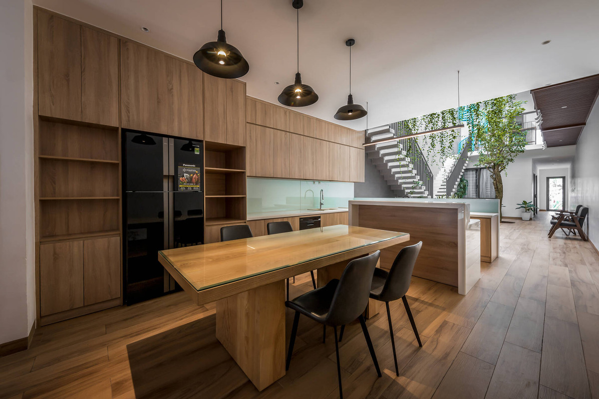 Bếp rộng rãi, bố trí hợp lý với tầm nhìn ra khoảng sân trong, giúp mẹ thư thái, dễ chịu hơn khi nấu nướng. Khoảng thông tầng giữa nhà kết nối với các phòng ngủ ở tầng trên. Nội thất sử dụng vật liệu gỗ chủ đạo tạo cảm giác ấm cúng, gần gũi.