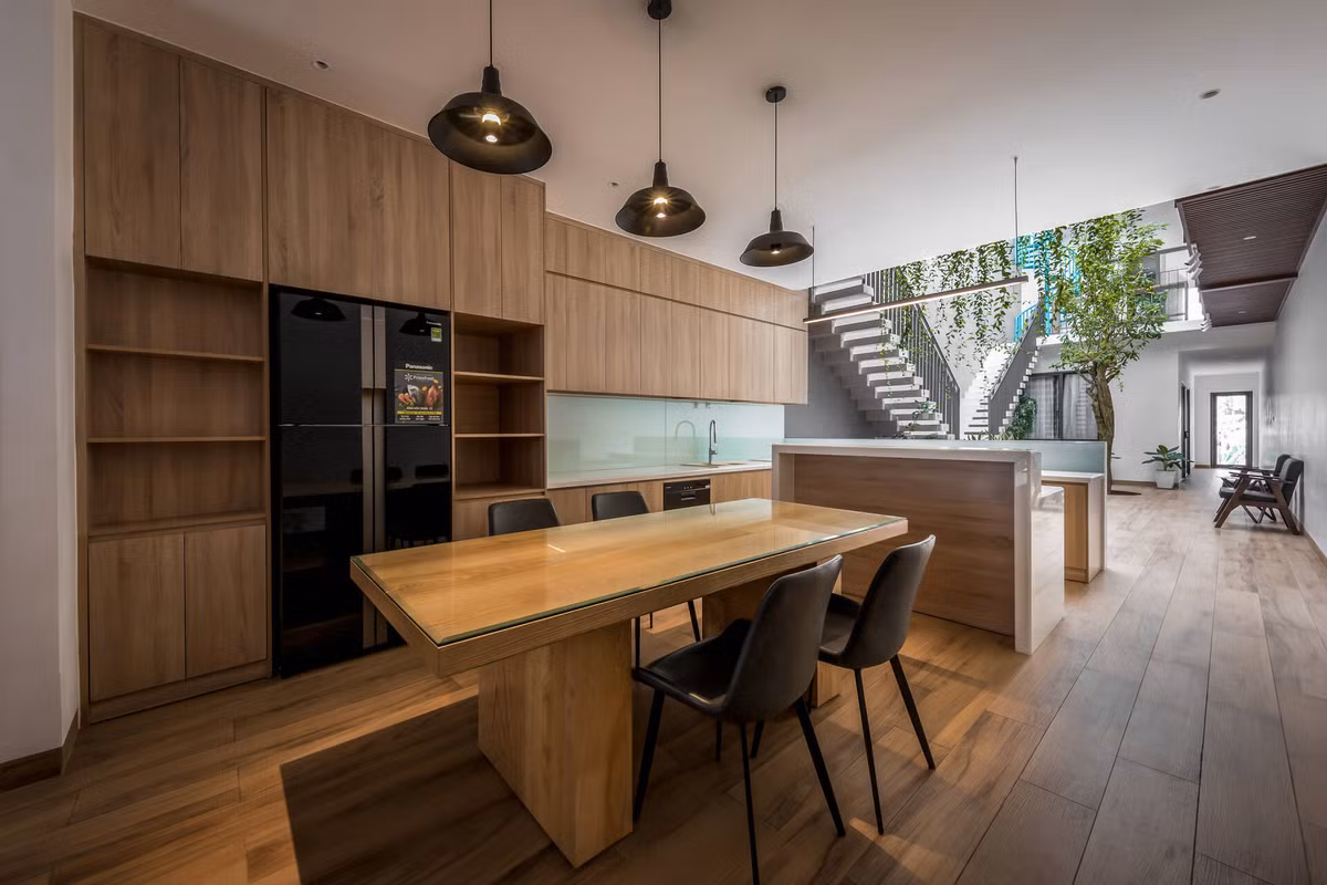 Bếp rộng rãi, bố trí hợp lý với tầm nhìn ra khoảng sân trong, giúp mẹ thư thái, dễ chịu hơn khi nấu nướng. Khoảng thông tầng giữa nhà kết nối với các phòng ngủ ở tầng trên. Nội thất sử dụng vật liệu gỗ chủ đạo tạo cảm giác ấm cúng, gần gũi.