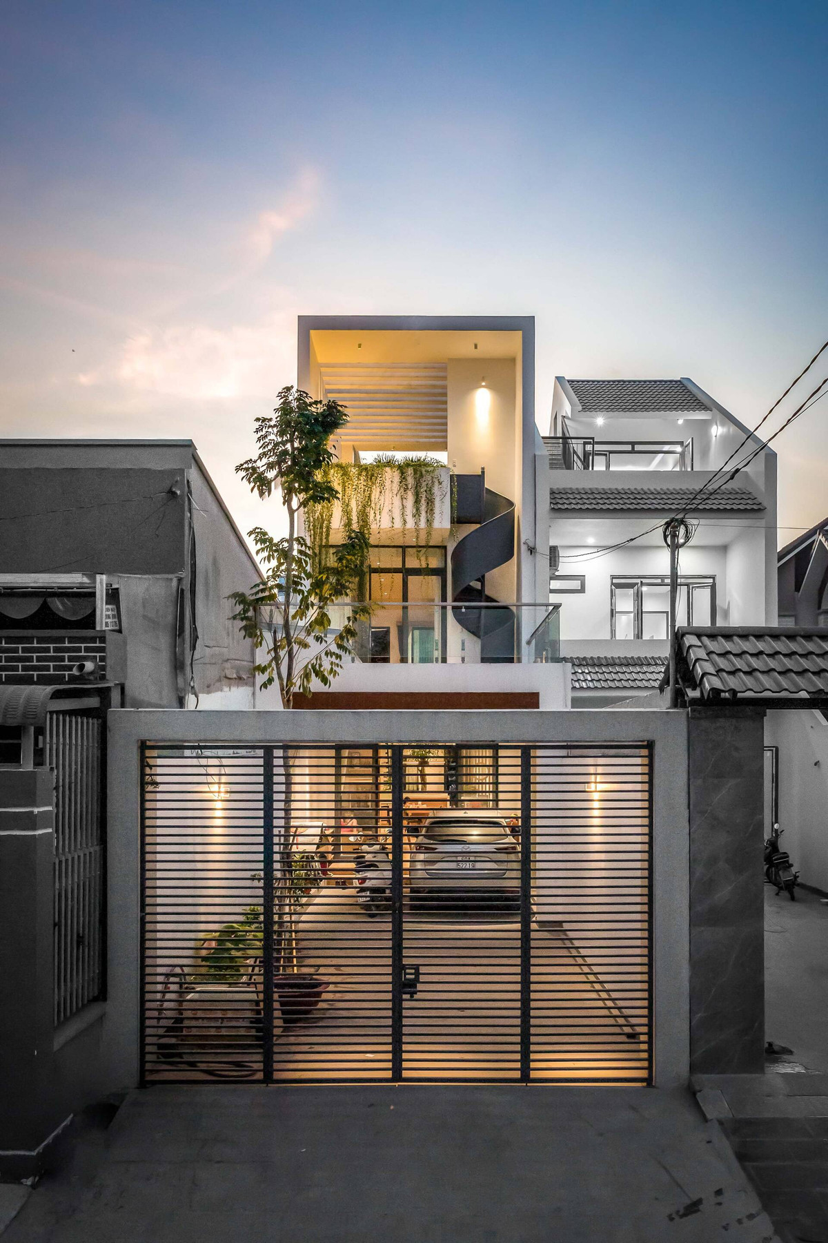  Ngôi nhà có cây cầu xanh ở Trảng Bom (Đồng Nai) là tổ ấm của một gia đình nhiều thế hệ. Gia chủ đặt ra bài toán là tạo một không gian tiện nghi, ấm cúng trên một khu đất hẹp và dài. Công trình có tổng diện tích là 240m2, được hoàn thành vào năm 2021. Khoảng sân lùi vào, vừa làm khu vực để xe, vừa như một khoảng đệm trước khi bước vào không gian chính