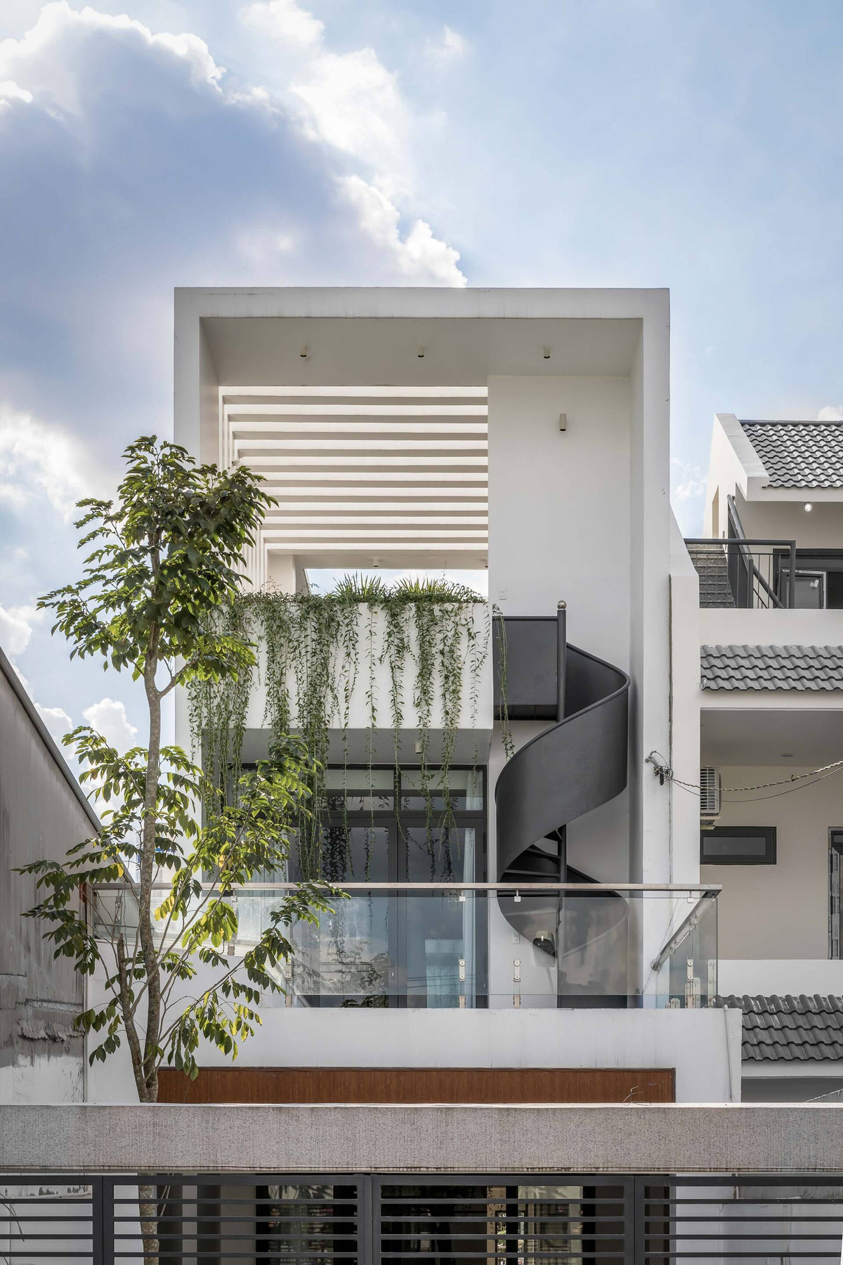 Mặt tiền được bao phủ bởi lớp cây xanh nhẹ nhàng, xanh mát. Công năng ngôi nhà bao gồm 3 tầng với 4 phòng ngủ. Trong đó tầng trệt là không gian của gara, phòng khách, bếp và phòng ngủ của bà. Phòng ngủ các con, bếp và các khu vực chức năng khác ở tầng trên.