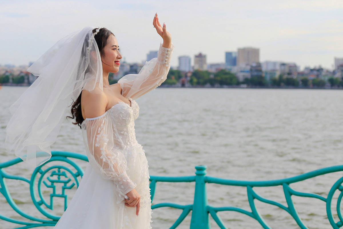 "Mình chọn hồ Tây làm nơi ghi hình ảnh cưới bởi không gian thoáng đãng, ánh sáng tự nhiên với cảnh sóng nước đằng sau. Ban đầu, mình dự định chụp cả ở 'cây cô đơn' nhưng rất tiếc cây đã bị đốn hạ. Khi mới yêu nhau, hai vợ chồng cũng thỉnh thoảng lấy nơi này làm chỗ hẹn hò", Mai (27 tuổi) cho biết. Chụp ngoài trời vào ngày nắng nóng 37 độ C, cô dâu có chút mệt nhưng hy vọng săn được cảnh đẹp vào cuối chiều.