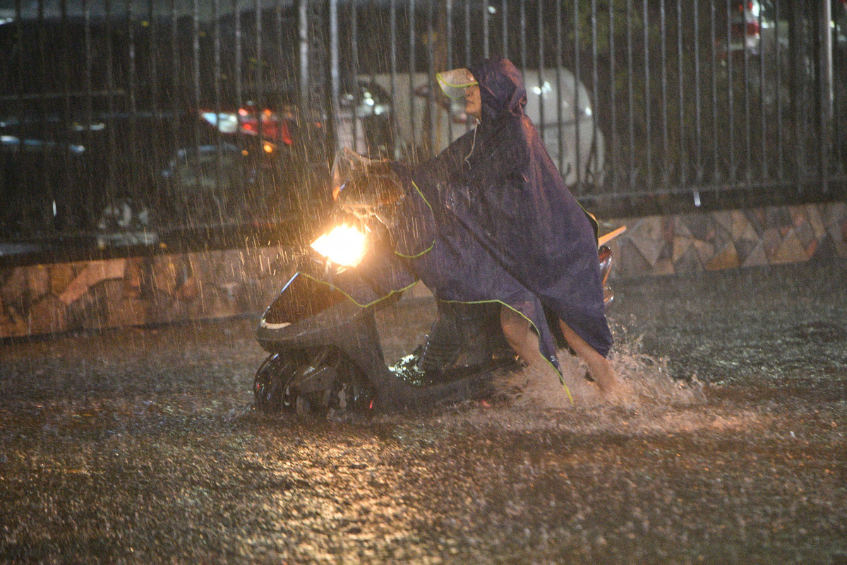 Một phụ nữ cố gắng dắt xe máy qua đoạn ngập. Ảnh: Thạch Thảo.