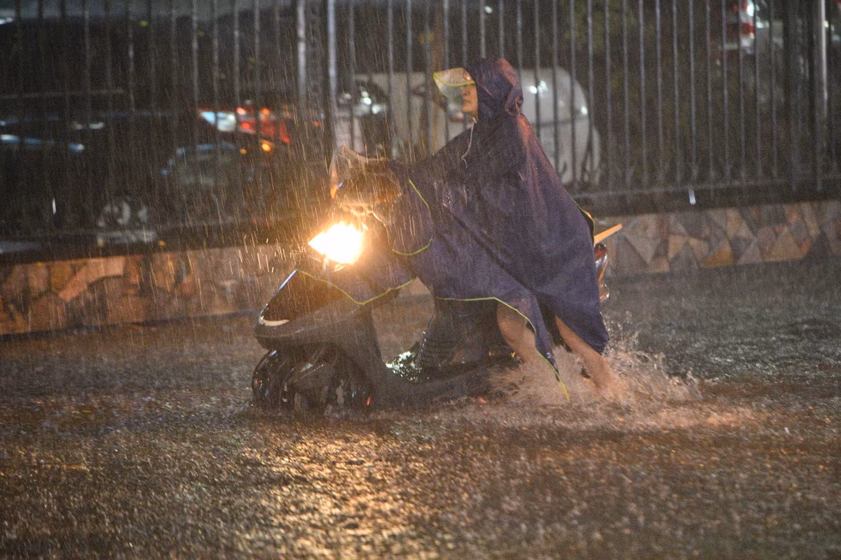 Một phụ nữ cố gắng dắt xe máy qua đoạn ngập. Ảnh: Thạch Thảo.