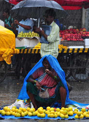 Một người bán trái cây ngồi trong cơn mưa như trút nước ở Mumbai, Ấn Độ. Mùa mưa bắt đầu từ tháng 6 đến tháng 9, chiếm khoảng 80% lượng mưa hàng năm của Ấn Độ, dễ gây lũ lụt tàn phá nước này.