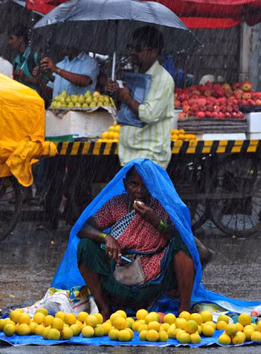 Một người bán trái cây ngồi trong cơn mưa như trút nước ở Mumbai, Ấn Độ. Mùa mưa bắt đầu từ tháng 6 đến tháng 9, chiếm khoảng 80% lượng mưa hàng năm của Ấn Độ, dễ gây lũ lụt tàn phá nước này.
