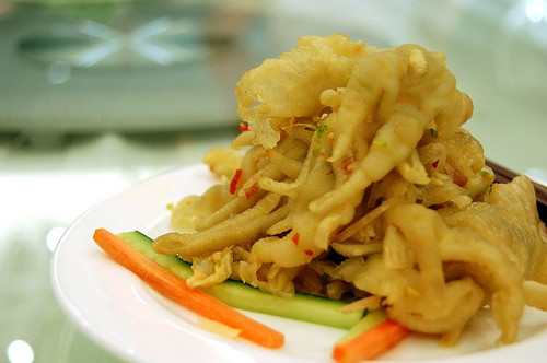 Cho chân gà vào tô, nêm mắm, chanh, hành, ớt, tỏi, đường, dùng tay bóp nhẹ cho gia vị thấm vào thịt. Cuối cùng bạn trộn chân gà với là húng, hành lá, ngò và gạo rang.