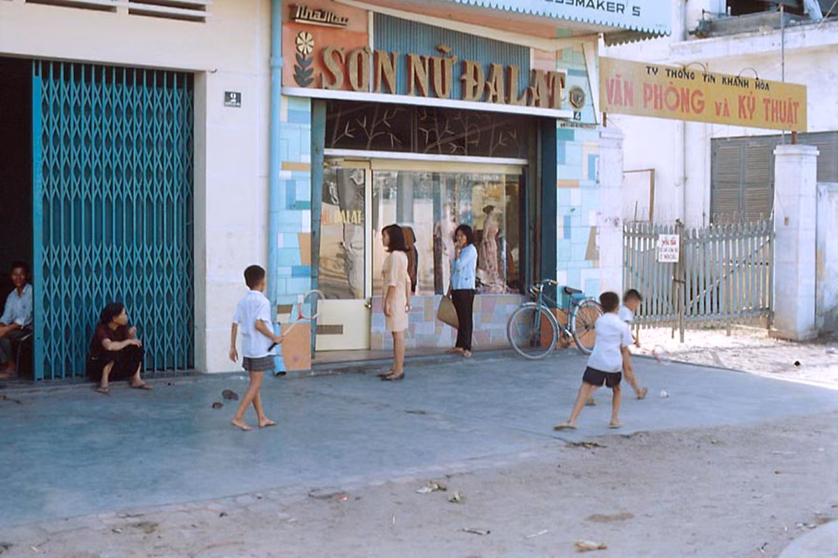 Những đứa trẻ chơi cầu lông bên ngoài tiệm may "Sơn nữ Đà Lạt", cạnh đó là cổng vào văn phòng của Ty thông tin Khánh Hòa.