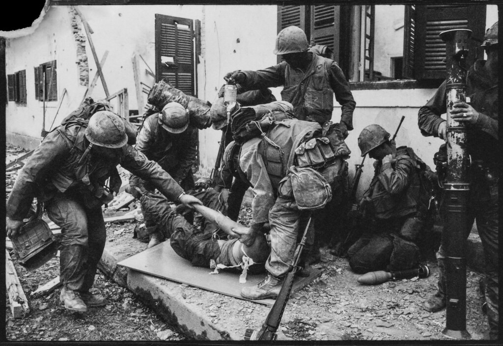 Blaine được đồng đội băng bó và chuyển lên chiếc cáng làm từ mảnh ván nhặt trên chiến trường.