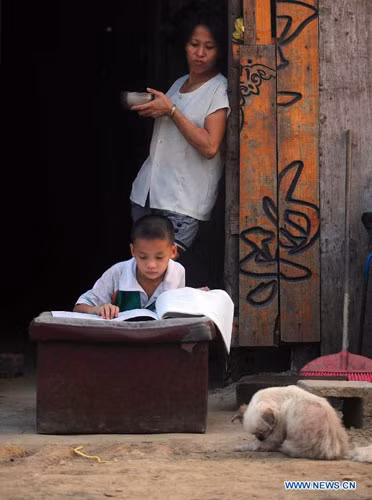 Bé trai Yang Peng, 8 tuổi ở làng Donghe, thành phố Baise, chăm chỉ làm bài tập với chiếc bàn học là chiếc đệm rách nát.