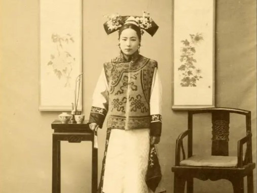  Có thể thấy người phụ nữ Mãn Châu này thuộc tầng lớp quyền lực. Cô ấy ăn mặc sang trọng và có một tẩu thuốc được chế tác tinh xảo trên bàn trà bên cạnh. Vào cuối thời nhà Thanh, hút thuốc (bao gồm cả thuốc phiện) đã trở thành thú giải trí của nhiều người giàu.