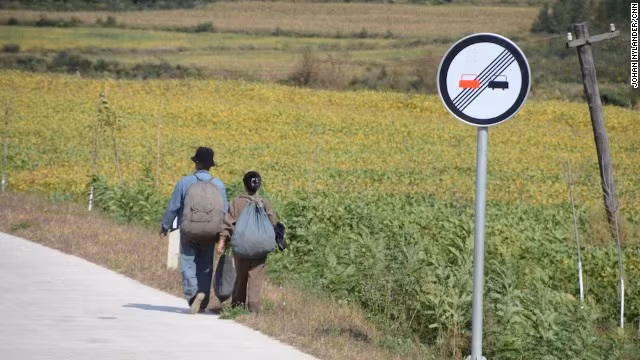 Một phụ nữ và một người đàn ông Triều Tiên đi bộ trên con đường quốc lộ. Hai bên đường là cánh đồng ngô rộng mênh mông. Đây là một trong số những bức ảnh của nhà báo Thụy Điển bị nhân viên an ninh Triều Tiên xóa.