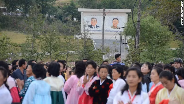 Người dân Triều Tiên tụ tập chờ xem các tay đua xe đạp về đích. Phía sau đám đông là chân dung của Chủ tịch Kim Nhật Thành và Kim Jong-il. Nhà báo Thụy Điển đã bị yêu cầu không chụp ảnh, ghi hình chân dung lãnh đạo Triều Tiên.