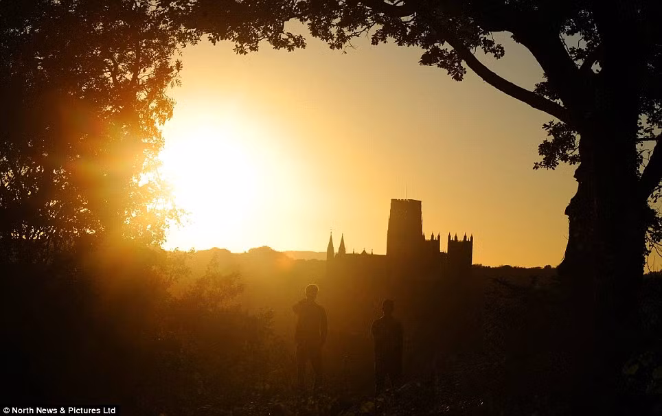 2 người đàn ông đứng ngắm cảnh mặt trời mọc huy hoàng, tráng lệ đằng sau lâu đài Durham Cathedral cổ kính.