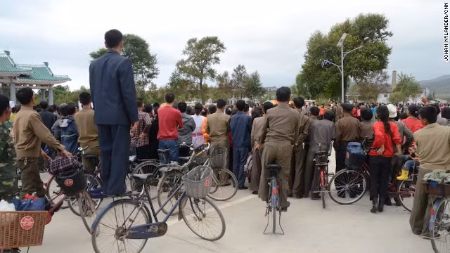 Người dân thành phố Rason đứng hẳn lên xe đạp để xem cuộc đua.