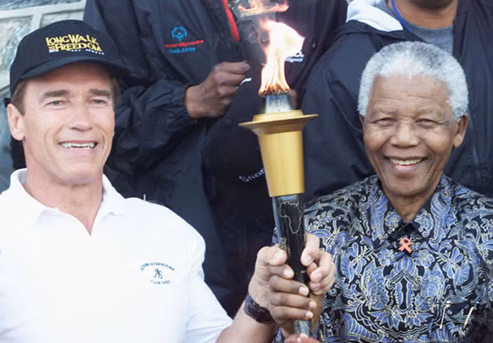 Cố Tổng thống Nelson Mandela cùng "Kẻ huỷ diệt" Arnold Schwarzenegger giữ biểu tượng "ngọn lửa hy vọng" tại một lễ kỷ niệm bên ngoài nhà tù mà ông Mandela từng bị giam giữ trên đảo Robben.