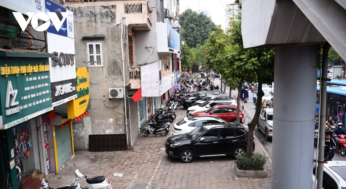 Ô tô chiếm vỉa hè trước cửa nhà người dân có nhân viên đeo băng đỏ thu vé trông xe.