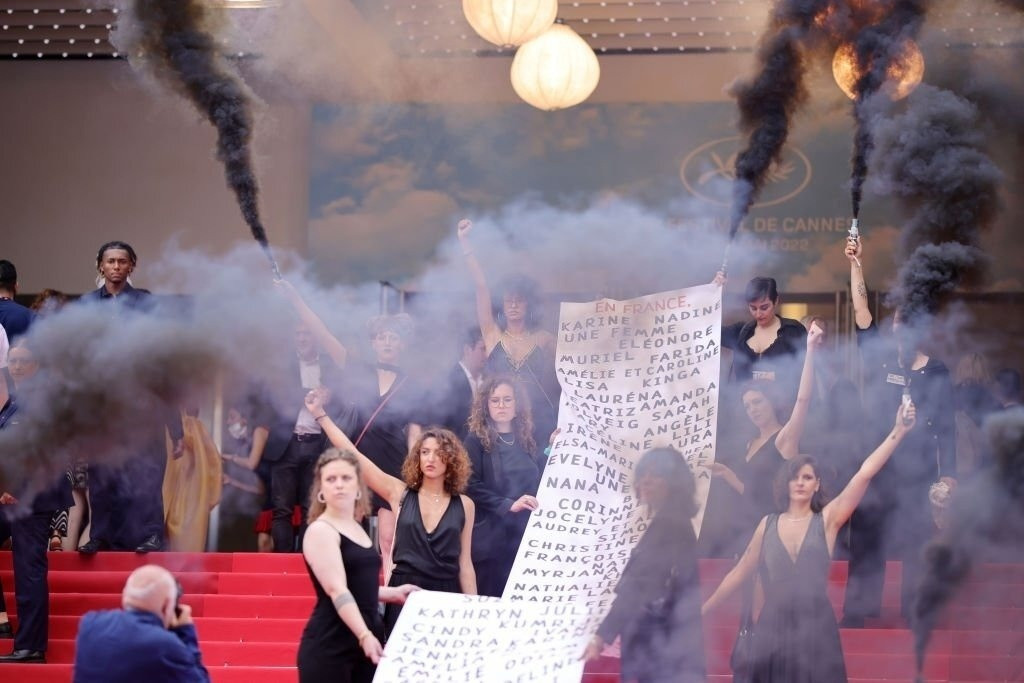 Vài ngày trước vụ của IU, thảm đỏ Cannes bị nhóm người bảo vệ nữ quyền gây náo loạn. Variety cho hay trong buổi công chiếu Holy Spider - phim kinh dị lấy nữ giới làm trung tâm, khoảng 12 phụ nữ mặc trang phục chỉnh tề, tụ tập trên cầu thang nối dài của Palais des Festivals và và giơ cao biểu ngữ, thả khói đen dày đặc. Bất ngờ thay, ban tổ chức không có động thái can thiệp, trái lại còn để phóng viên thoải mái chụp ảnh, quay phim nhóm người này. Ảnh: Cannes Festival Film.