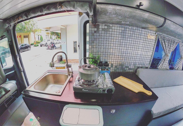 Vì diện tích sử dụng chỉ 6m2 nên phải tận dụng tối đa không gian và các đồ vật trong xe có nhiều công dụng nhất”, anh Sơn chia sẻ. Trong khu bếp, vợ chồng anh Sơn sử dụng một chiếc tủ lạnh chạy nguồn 12V, dung tích 50l giúp bảo quản thức ăn. Và bếp ga mini được sử dụng trong căn bếp này để tiện việc mang ra ngoài nấu nướng khi cần. Bồn rửa tay và hoa quả được đặt đối diện bếp để tiện sử dụng. Dưới bồn là một bình nước 110l để cung cấp nước cho cả xe. Từ bình nước này, đôi vợ chồng trẻ thiết kế một đường nước dẫn tới vòi xịt cũng như vòi hoa sen ở đằng sau. Đường điện được bố trí phía đối diện và tách biệt với đường nước.