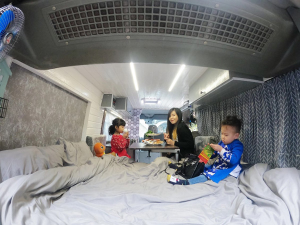 Vợ chồng trẻ đã mua một chiếc xe cũ về cải tạo. Diện tích vỏn vẹn chưa đến 7m2 nhưng sau khi cải tạo chúng rất tiện nghi: có đủ giường, tủ, bếp, vệ sinh, tắm rửa, bàn ăn, bồn rửa tay… đủ phục vụ cho cả nhà trên các chuyến đi dài. Chiếc giường đủ cho 3 mẹ con có thể thoải mái nằm. “Căn nhà” này được thiết kế với 2 tông màu chính là màu trắng và màu ghi. Phần bếp được bố trí ở phía lái gần cửa sổ và được trang bị thêm 1 chiếc quạt thông gió để khi nấu nướng không bị ám mùi. “Khu vực bếp cũng đóng vai trò như một cái bàn làm việc, có thể dọn đi và để laptop.