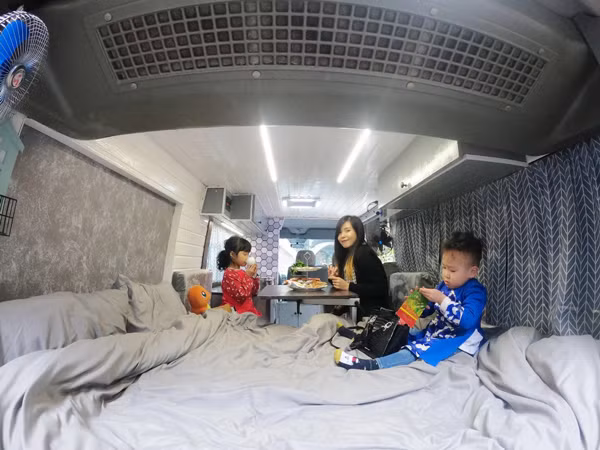 Vợ chồng trẻ đã mua một chiếc xe cũ về cải tạo. Diện tích vỏn vẹn chưa đến 7m2 nhưng sau khi cải tạo chúng rất tiện nghi: có đủ giường, tủ, bếp, vệ sinh, tắm rửa, bàn ăn, bồn rửa tay… đủ phục vụ cho cả nhà trên các chuyến đi dài. Chiếc giường đủ cho 3 mẹ con có thể thoải mái nằm. “Căn nhà” này được thiết kế với 2 tông màu chính là màu trắng và màu ghi. Phần bếp được bố trí ở phía lái gần cửa sổ và được trang bị thêm 1 chiếc quạt thông gió để khi nấu nướng không bị ám mùi. “Khu vực bếp cũng đóng vai trò như một cái bàn làm việc, có thể dọn đi và để laptop.