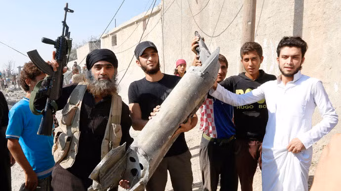 Một chiến binh IS (người giơ súng lên) cùng người dân địa phương khoe chiến lợi phẩm là mảnh vỡ một máy bay.