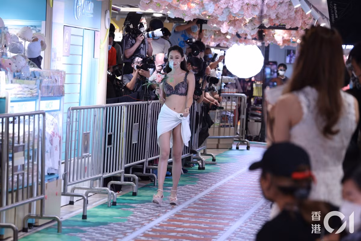 Các người đẹp mặc trang phục gợi cảm, đeo khẩu trang và trình diễn ở trung tâm thương mại. Sự kiện do TVB tổ chức được nhận xét làm rẻ rúng hình ảnh của các người đẹp xuất thân từ cuộc thi nhan sắc.