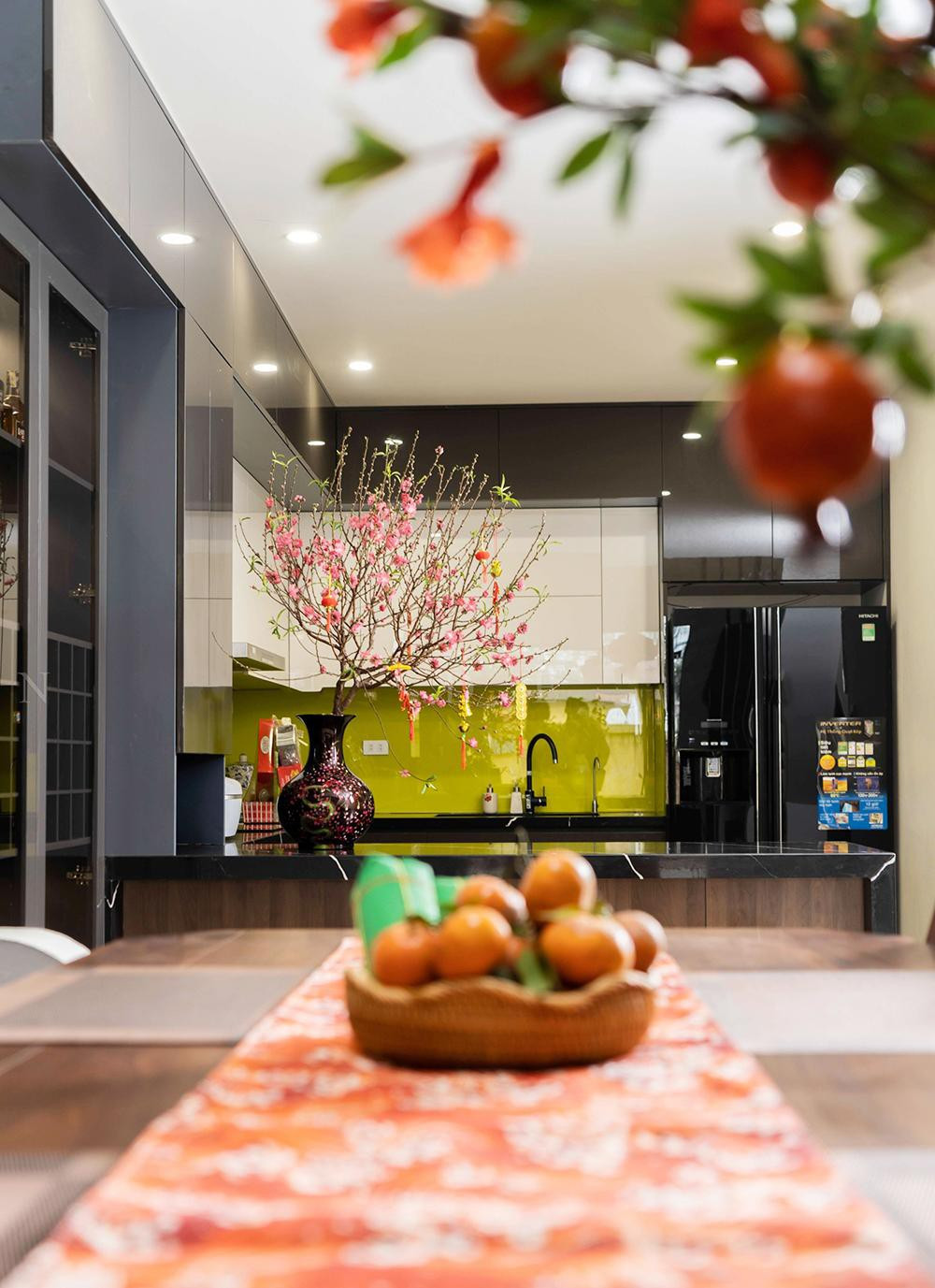 Không gian bếp hiện đại và tiện nghi. Gia chủ sử dụng khăn trải bàn màu cam kết hợp với cành đào, bánh chưng xanh trang trí khu vực bếp để không gian ở đây rực rỡ sắc xuân và khiến nhiều người đùa rằng ngôi nhà này xây chỉ để ăn Tết.