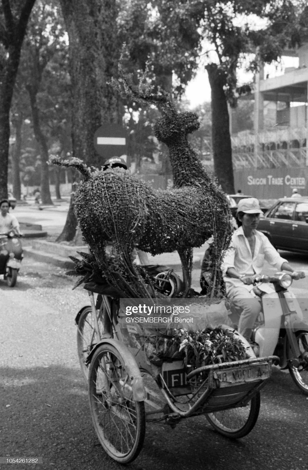 Người lái xích lô chở cây cảnh hình con hươu đi qua công trường xây dựng tòa nhà Saigon Trade Center, 37 Tôn Đức Thắng.