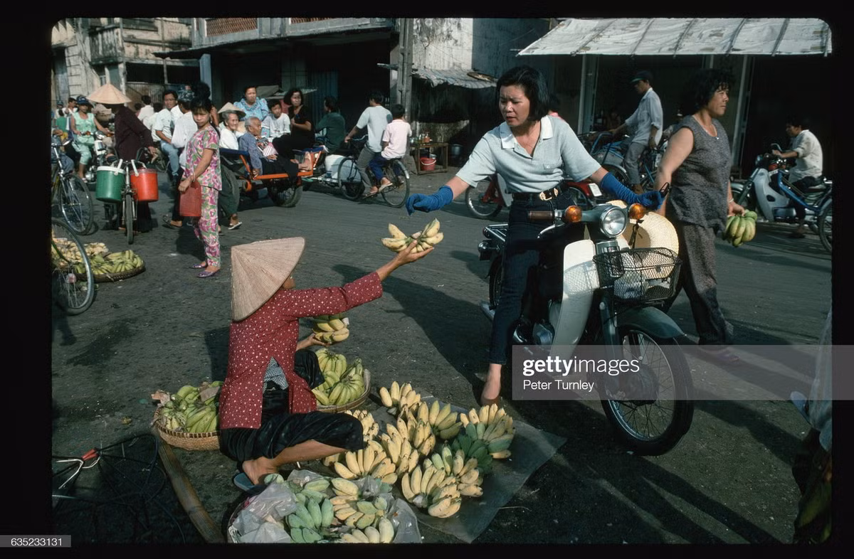 Người phụ nữ ngồi Honda sà vào quầy bán chuối bên lề đường.