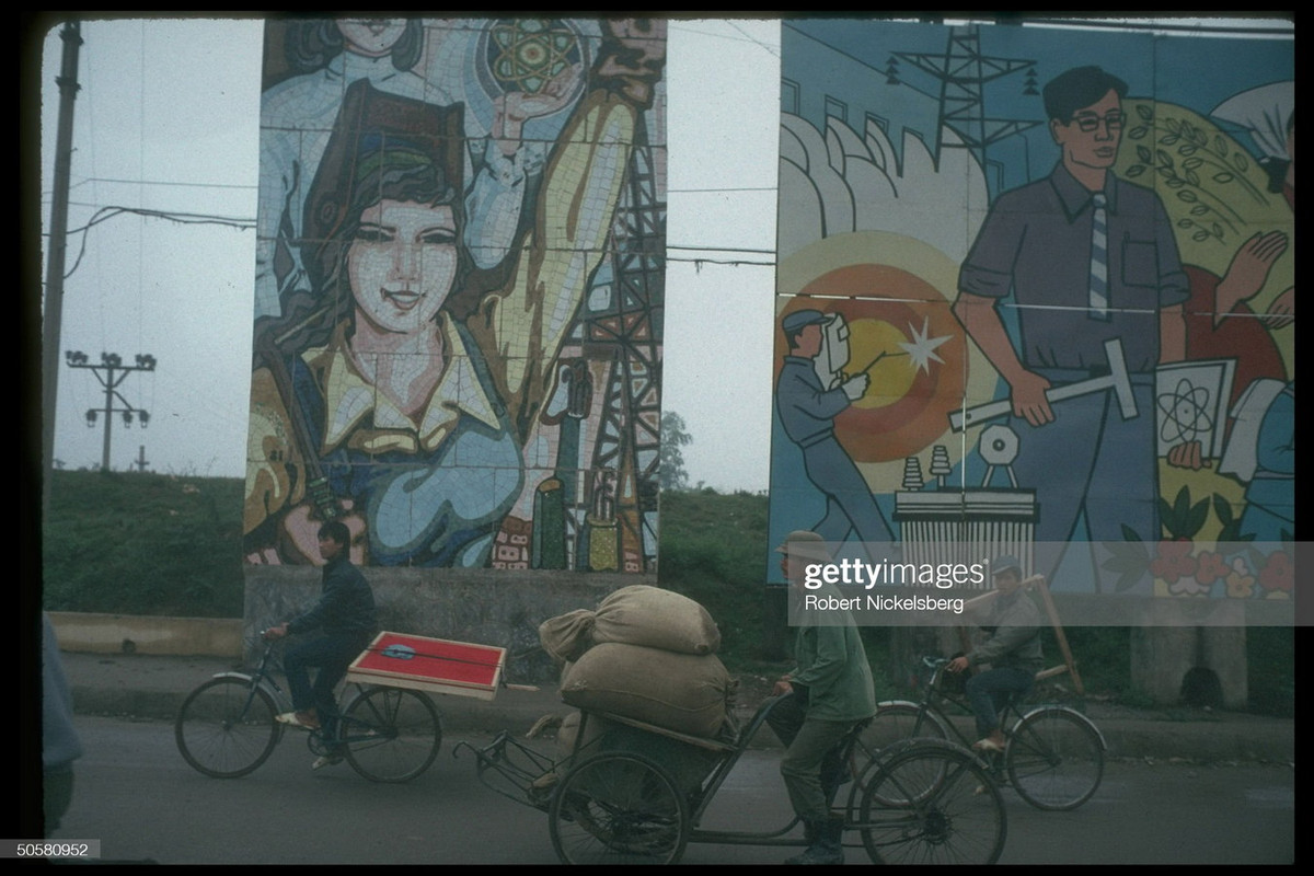 Xe đạp và xích lô chở hàng ngang qua những bức tranh cổ động.