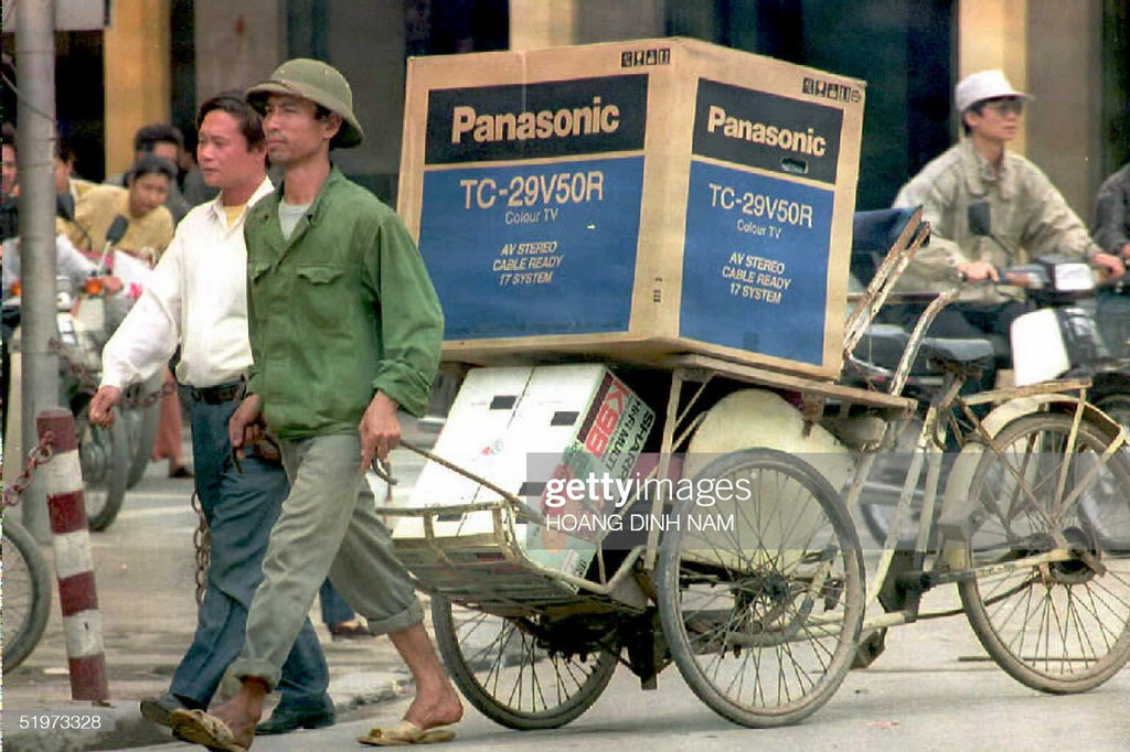 Một người lái xích lô kéo thùng TV và máy cassette để giao cho một khách hàng, 19/4/1995. ở Hà Nội năm 1995, hàng điện tử Nhật Bản đang tràn ngập thị trường do thu nhập bình quân của người dân liên tục tăng cao vào năm qua, và hàng tiêu dùng xa xỉ không còn nằm ngoài tầm với. Ảnh: Hoang Dinh Nam/Getty Images.