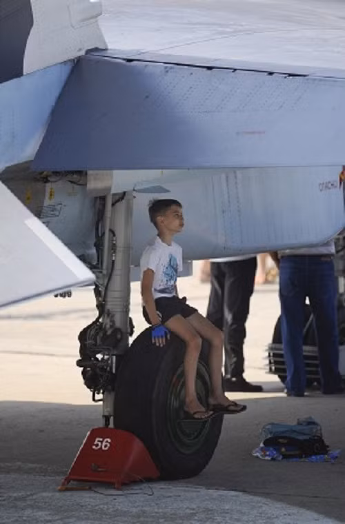 Một du khách nhí tham gia lễ kỷ niệm đang tranh thủ tránh nắng bên dưới một chiếc máy bay chiến đấu.