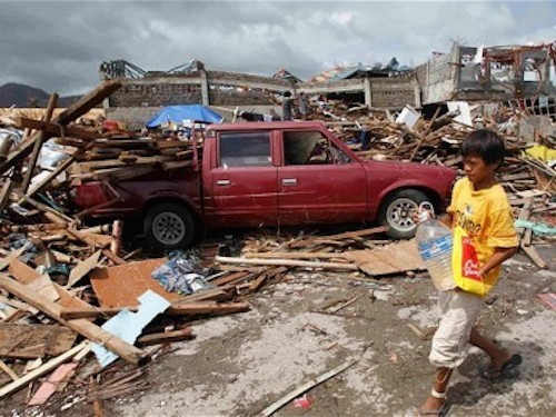 Một cậu bé cầm bình đi tìm nước uống giữa đống đổ nát tại thành phố Tacloban - Ảnh: Reuters