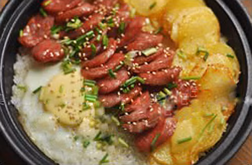 Cơm trộn khoai tây, xúc xích. Phi hành tây và tỏi vàng giòn rồi vớt ra, cho khoai tây vào rán vàng, tiếp đến cho xúc xích vào rán đến khi vừa chín, cạnh chuyển màu nâu là được. Khi cơm vừa chín tới, bạn mở nắp nồi rồi xếp xúc xích và khoai tây vào. Sau đó, đập trứng vào góc còn lại, đậy nắp rồi nấu ở lửa nhỏ. Khi trứng đã chín, bạn mở nắp nồi, rắc thêm hành lá và mè lên trên.