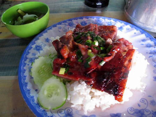  Cơm thịt heo. Cơm thịt heo (bai sach chrouk) xuất hiện ở mọi góc phố trên khắp đất nước Campuchia vào mỗi sáng sớm. Đây là một trong những món ngon và đơn giản nhất tại quốc gia này. Thịt heo thái mỏng, được nướng qua than hồng để giữ độ ngọt tự nhiên của thịt. Người ta còn ướp thịt heo với nước cốt dừa hoặc tỏi, tùy thuộc vào mỗi vùng. Cũng bởi điều này mà bai sach chrouk mang nhiều hương vị khác nhau. Bai sach chrouk còn gồm có cơm tấm, dưa chuột và củ cải, kèm theo gừng và một bát nước dùng với hành tươi và hành khô phi thơm nức mũi.