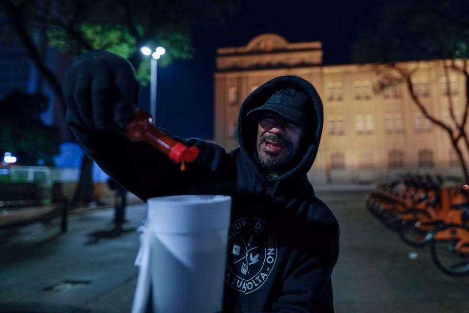 Rodrigo, một người vô gia cư 14 năm, thêm sốt ớt cay cho chén súp trong một đêm lạnh giá ở Sao Paulo vào ngày 29/7. Nhiệt độ giảm và thời tiết lạnh khiến nhiều người vô gia cư tại Brazil phải nhanh chóng tìm nơi trú ẩn và thức ăn ấm để giữ an toàn.