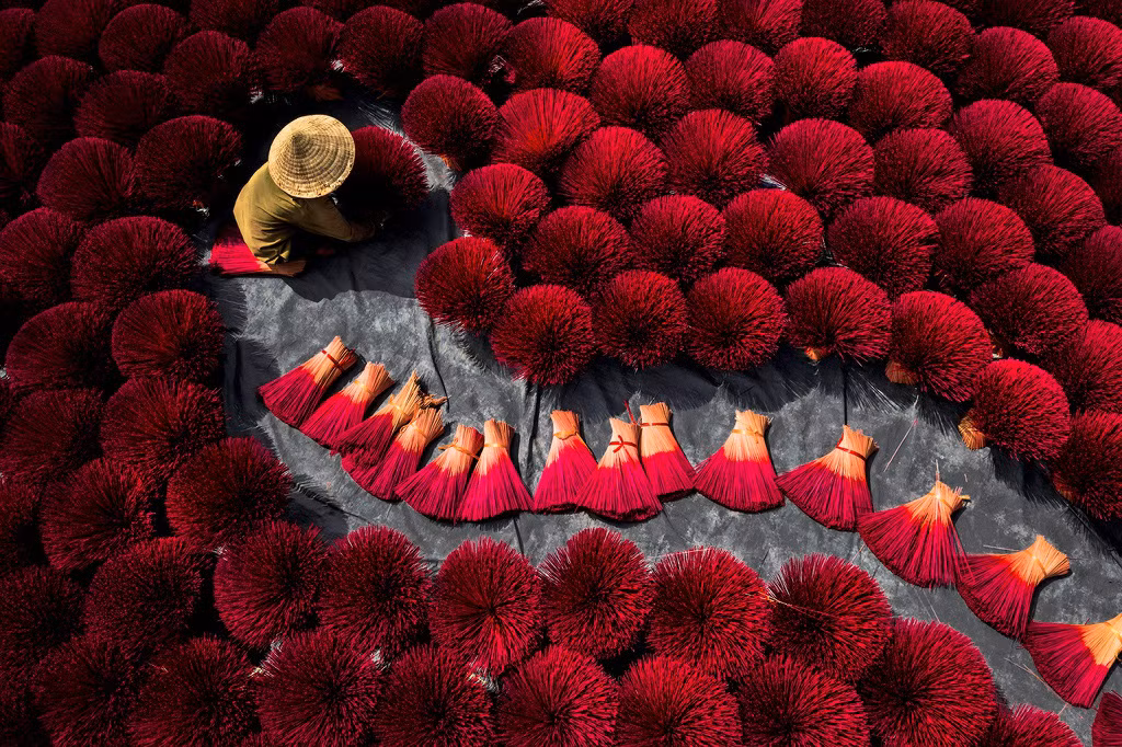 Ở ngoại ô Hà Nội, hình ảnh người lao động được bao quanh bởi các bó nhang đỏ tạo thành cảnh tượng ma mị, đầy sức hút. Ảnh: Thach Pham Ngoc.