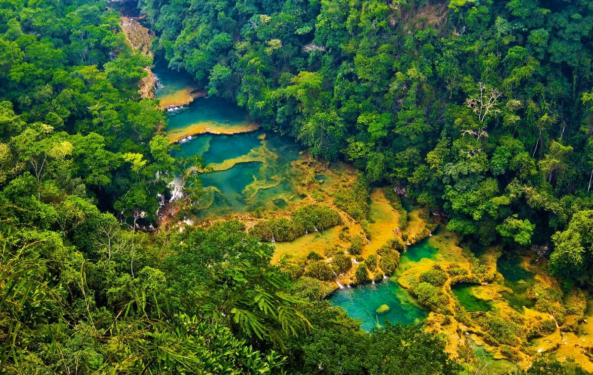  1. Semuc Champey. Semuc Champey là một loạt các cây cầu tự nhiên và hang động đá vôi nằm ở miền trung Guatemala. Điểm đến biệt lập này là nơi du khách đắm mình trong làn nước trong vắt, mát lạnh của những hồ bơi tự nhiên tuyệt đẹp, giữa khung cảnh núi rừng hùng vĩ, hoang sơ.
