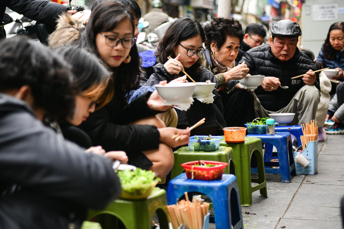 Tại vỉa hè của phố Xã Đàn, một gánh bún riêu thu hút được nhiều thực khách. Để tiết kiệm diện tích, quán không sử dụng bàn mà thay vào đó là dùng ghế, xếp thành hàng dài.