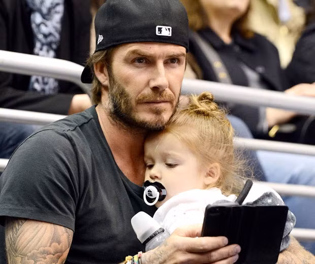 Harper ngậm ti giả, nằm ngoan ngoãn trong lòng bố Beck khi hai bố con đi xem bóng rổ.