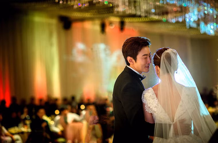 Chú rể tay ôm eo, miệng thì thầm vào tai cô dâu.