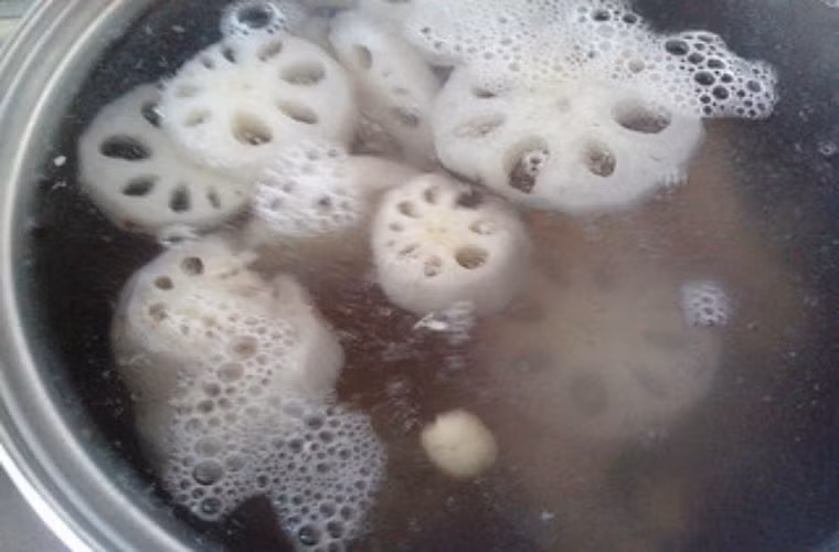 Đợi nước xương sôi, cho lạc và củ sen vào nồi xương ninh cùng.