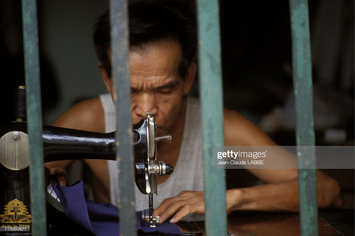 Người thợ may cao tuổi phía sau ô cửa sổ.