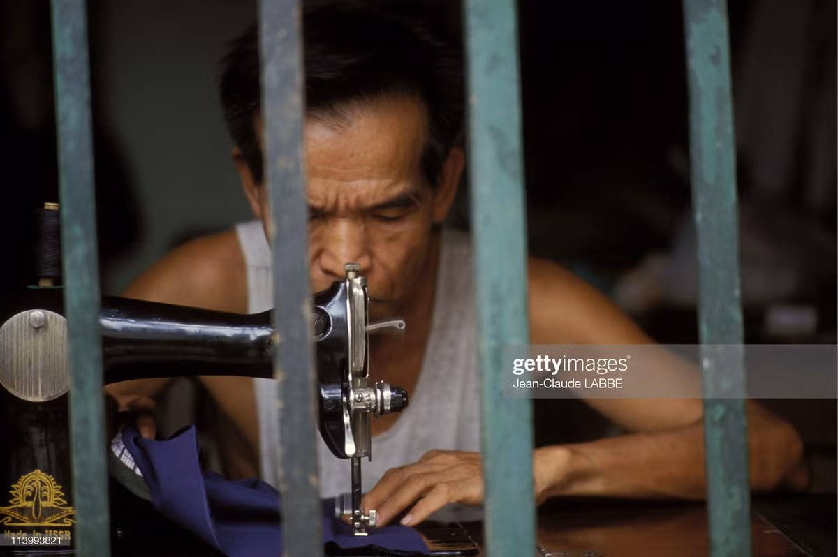 Người thợ may cao tuổi phía sau ô cửa sổ.