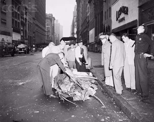 Nhân viên công lực xem xét một phần còn sót lại của chiếc máy bay ném bom bị rơi trên mặt đường.