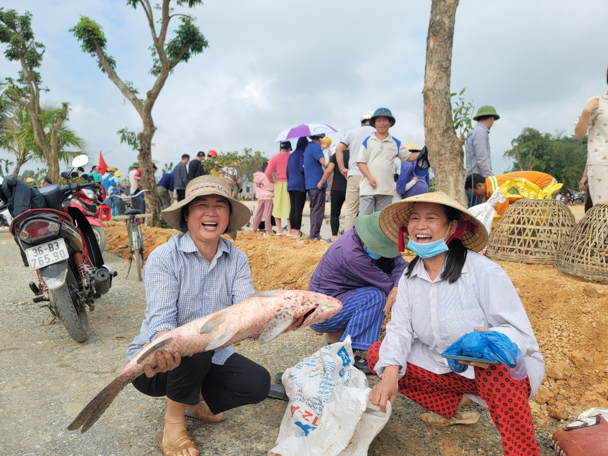 Những người phụ nữ đứng trên bờ vui vẻ đón cá của người thân bắt được.